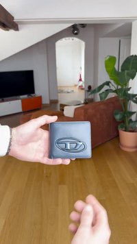 Μαύρο δερμάτινο πορτοφόλι με ανάγλυφο λογότυπο, ορθογώνιο σχήμα, ομαλή υφή και αντίθετη ραφή. Κρατείται με το χέρι σε έναν καλά φωτισμένο εσωτερικό χώρο.