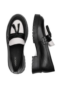Černé kožené mokasíny s bílým koženým špičkou, zdobené třásňovým detailem a silnou gumovou podrážkou. Hladká textura s kontrastními designovými prvky.