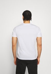 Balta trumpa rankovė t-shirts su apvaliu kaklu, pagaminta iš lygaus medvilnės. Medžiaga atrodo lengva; nematoma jokių raštų ar akcentų.