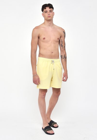 Pantaloni da bagno gialli con vita elasticizzata e cordoncino, abbinati a sandali neri con fasce testurizzate.