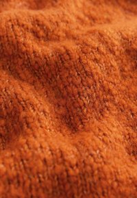 Tejido de punto texturizado en vibrante color naranja, con una superficie suave y peluda, que presenta patrones de costura visibles y variaciones de profundidad.