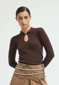 Brown long-sleeve ribbed top featuring a collar and a keyhole detail at the chest, paired with a brown fringed skirt.