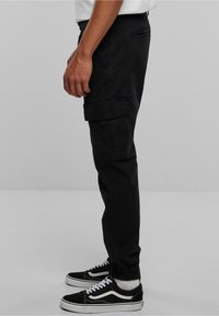 Pantalon cargo noir avec poches latérales, ourlets fuselés et une texture lisse. Associé à des baskets noires et blanches au design classique.