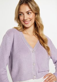 Cardigan viola chiaro con texture a coste, design a V e quattro bottoni decorativi. Materiale morbido; presenta una silhoutte aderente.