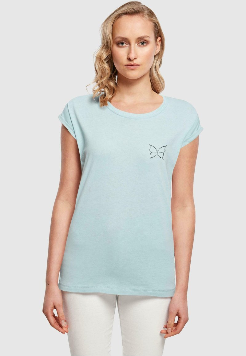 Lys blå kortermet t-skjorte med rund hals og en liten brodert sommerfugl-design på venstre brystområde.