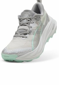 Scarpa atletica grigio chiaro con tomaia in mesh, dettagli verde menta, suola grigia testurizzata e particolari riflettenti. Presenta chiusura con lacci e linguetta.