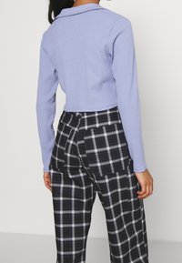 Ljuslila ribbad långärmad tröja med krage, ihop med svarta och vita rutiga vida byxor som har fickor och en avslappnad passform.