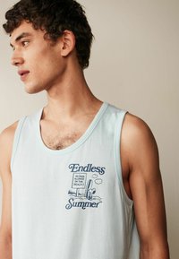 Ljusblå linne i mjukt material med rundad halsringning. Har en grafisk tryck i marinblått som säger "Oändlig Sommar" och ett strandskylt.