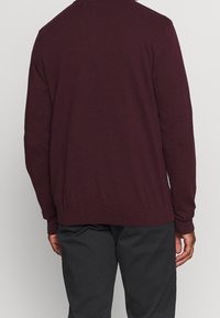 Burgundský pletený kardigan s kulatým výstřihem, žebrovanými manžetami a lemem. Měkká textura, střední tloušťka, pohled zezadu s minimálními designovými detaily.