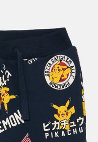 Námornícke modré teplákové nohavice vyrobené z bavlny, s grafikou Pikachu a slogany ako "Musíš ich všetkých chytiť!" v živých farbách a japonskom texte.
