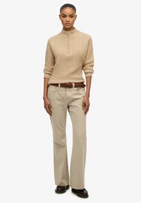 Beżowy sweter w warkoczowym splotem z ćwierć zamkiem, w połączeniu z jasnymi khaki spodniami w fasonie dzwonów i brązowym plecionym paskiem. Czarne buty dopełniają zestaw.