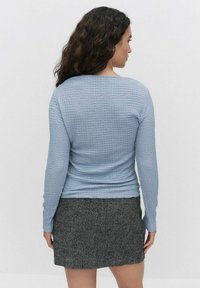 Ljust blå texturerad långärmad topp som matchas med en kjol i svart och vit houndstooth-mönster; synliga sömmar och figursydd siluett.