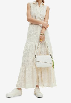 Ärmelloses cremefarbenes Spitzen-Maxikleid mit Kragen, weiße Sneaker, weiße Handtasche mit geflochtenem Griff und bunte Armbänder am Handgelenk des Models.
