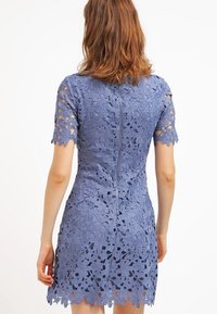 Vestido de encaje en azul claro, con mangas cortas, recortes florales y un dobladillo con forma de pico, y un detalle de cremallera central en la parte posterior.