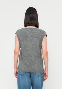 Grijze mouwloze gebreide top met een ronde halslijn en subtiele textuur, gecombineerd met losse blauwe jeans, gezien vanuit de achterkant.
