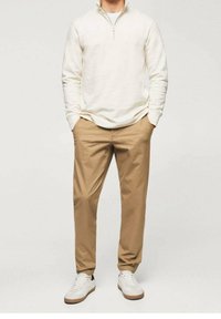 Polaire crème zippée, pantalon kaki fuselé, et baskets blanches avec des accents beiges. Tenue décontractée aux textures lisses et aux couleurs neutres.