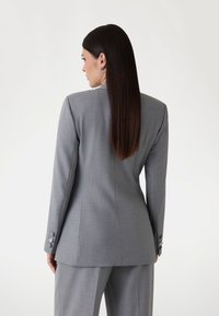 Blazer grigio chiaro con lapels affilati, design a schiena aderente e polsini abbottonati. Texture liscia e silhouette su misura, abbinato a pantaloni coordinati.