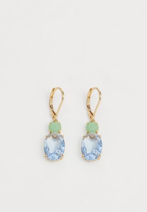 Boucles d'oreilles pendantes en or avec une petite pierre ovale verte au-dessus d'une pierre précieuse facettée bleue plus grande sur un fond blanc.