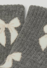 Graue gestrickte Socken mit einem Muster aus cremfarbenen Schleifen. Weicher Stoff, gerippte Struktur und ein besonderer Fokus auf den umrissenen Details der Schleifen.