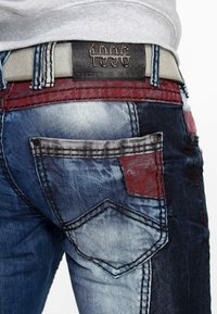 Denim jeans met een patchworkontwerp in tinten blauw en rood. Bevat contrasterende stiksels, metalen hardware en een leren tailleband met merklogo.