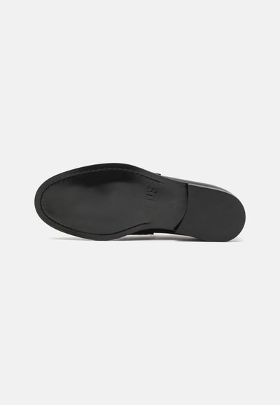 Semelle de chaussure en cuir noir avec texture lisse, forme de bout arrondi et logo discret embossé sur la surface inférieure.