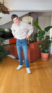Fleecetröja med dragkedja i ljusgrått, blå jeans i denim med rak skärning och vita sneakers; inomhusmiljö med trägolv.