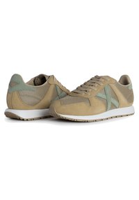 Zapatillas deportivas beige con parte superior de malla y acentos de ante, detalles en verde claro, punta redonda y suela de goma con dibujo.
