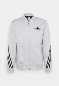 White jacket with a zip closure, ribbed collar, and black striped accents on sleeves. Features an embroidered black logo on the chest.