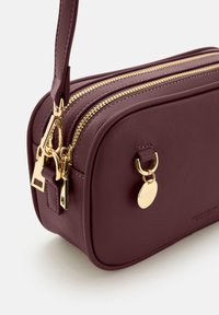 Burgunderfarbene Ledertasche mit zwei goldenen Reißverschlüssen, glatter Textur, rechteckiger Form, hängendem goldenen Etikett und einem kurzen Griff.