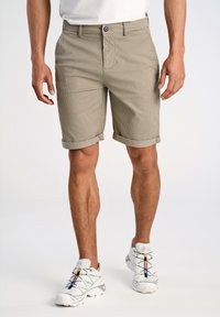 Pantalones cortos texturizados en tono beige con dobladillos enrollados. Bolsillos frontales y cierre de botón. Combinados con zapatillas blancas con detalles de color.