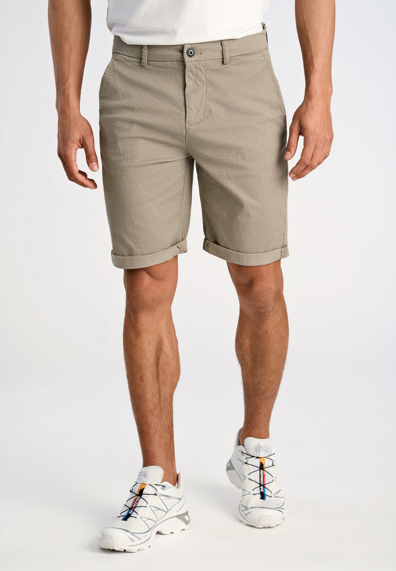 Pantalones cortos texturizados en tono beige con dobladillos enrollados. Bolsillos frontales y cierre de botón. Combinados con zapatillas blancas con detalles de color.