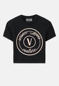 Juodas medvilnės marškinėliai su dideliu smėlio spalvos apvaliu logotipu, kuriame nurodyta "Versace Jeans Couture" ir centrinis elegantiškas „V“. Trumpomis rankovėmis.