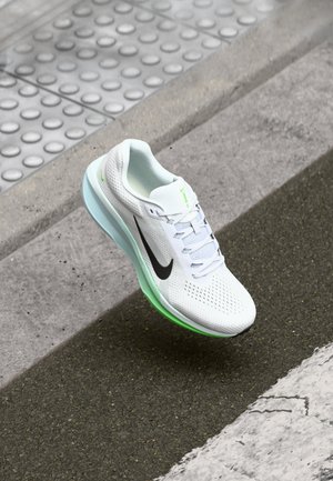 Zapatilla deportiva blanca con parte superior de malla, swoosh negro y suela verde translúcida. Presenta cordones y una superficie texturizada para mayor tracción.