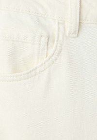 Gros plan sur un tissu denim blanc cassé montrant une poche avant, une passants de ceinture, et des coutures doubles sur un jean.