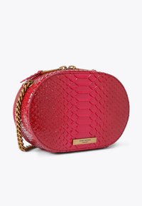 Borsa ovale rossa con texture in pelle di rettile, dotata di tracolla a catena e un'etichetta in tono oro. Finitura liscia e lucida con chiusura a zip.