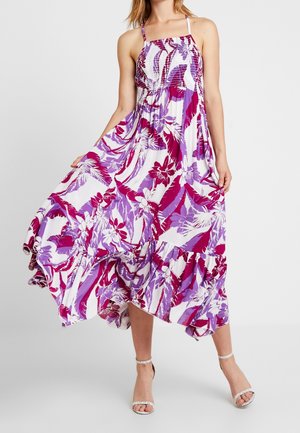 Robe maxi à motifs floraux violets et blancs éclatants, avec un corsage smocké, des bretelles halter et un ourlet à volants. Le tissu fluide apporte de la texture.