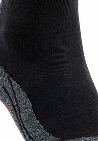 Svart strumpa med en texturerad grå detaljer vid ankeln, med röda inslag. Materialet verkar ribbade och elastiska för komfort.