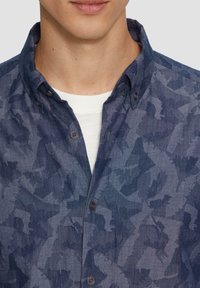 Blauw patroon overhemd met een casual kraag. De stof heeft een gestructureerd, abstract ontwerp in verschillende tinten blauw.