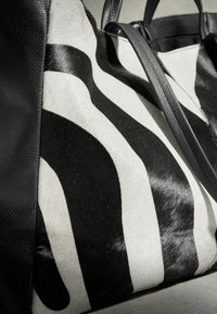 Sac fourre-tout en cuir rayé zèbre noir et blanc avec des anses et des finitions en cuir noir, présenté en gros plan.