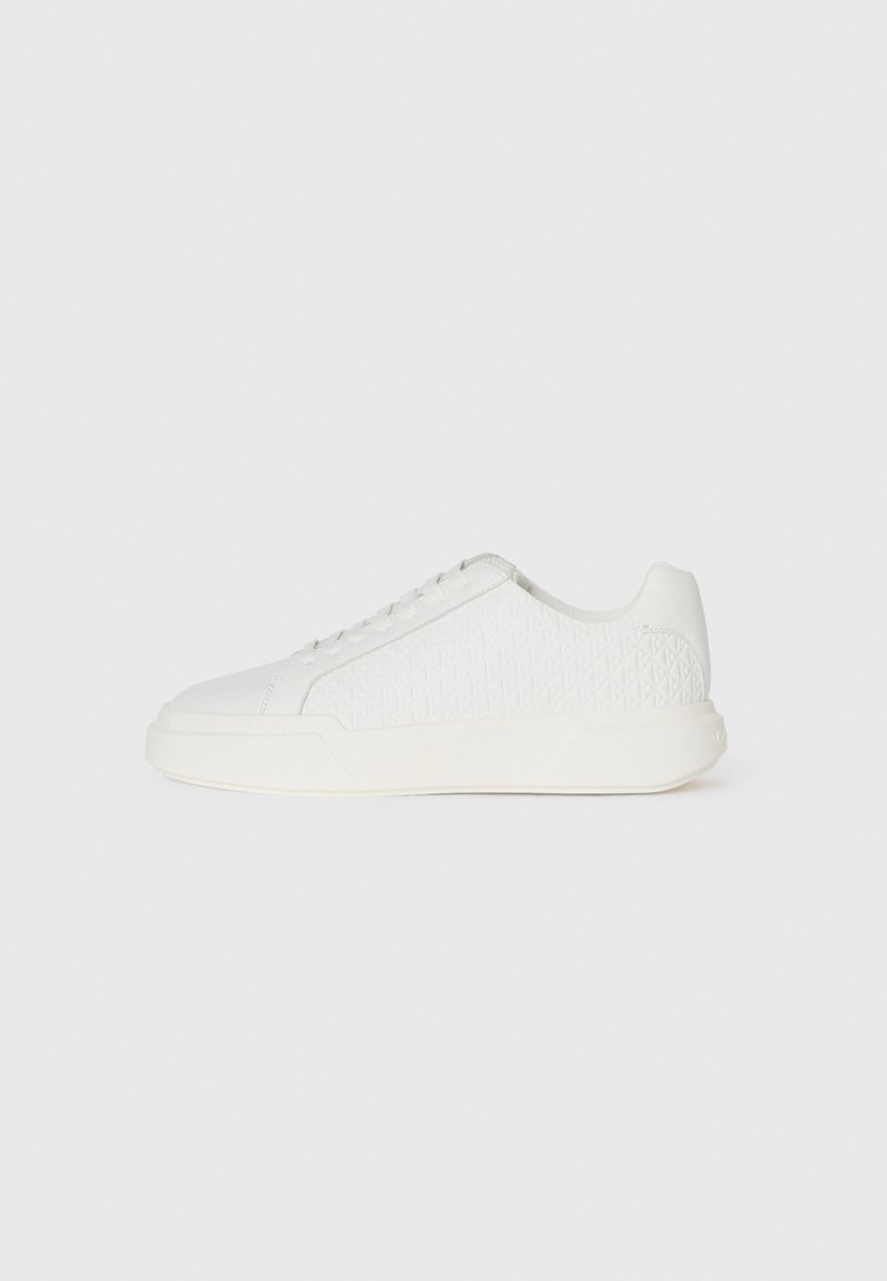 Hvit sneaker med en teksturert overdel som har et diamantmønster, rund tupp og flat gummisåle. Snøring med minimale detaljer.