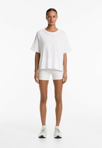 Tricou alb cu mânecă scurtă, realizat dintr-un material moale, asortat cu pantaloni scurți albi, mulati. Ținuta este completată cu adidași albi și șosete până la gleznă.