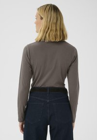 Langärmliges, braunes Oberteil aus weichem Stoff, kombiniert mit dunkelblauen Jeans. Hat ein schlichtes Design und eine taillierte Silhouette.
