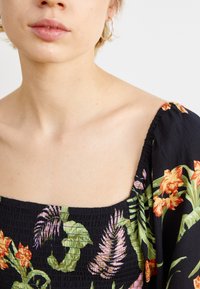 Mustmustrite mustriga ja ruudulise kaelusega musta lillemustriga topp, kus on erksad oranžid, roosad ja rohelised kujundid; tekstureeritud kangas, millel on kokku volditud varrukad.