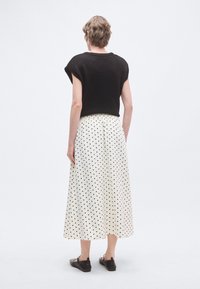 Μαύρο κοντομάνικο cropped πουλόβερ με στρογγυλή λαιμόκοψη, σε συνδυασμό με λευκή midi φούστα με πουά σχέδια. Το σύνολο διαθέτει ρευστό σχέδιο.