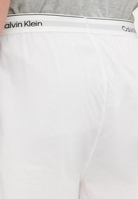 Calvin Klein baltās kokvilnas šortos ar elastīgu jostu. Jostas augšējā malā ir melnā un pelēkā krāsā izveidots logo. Mīksta tekstūra.
