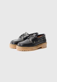 Schwarze Lederschuhe mit runder Zehenform, Schnürverschluss vorne und beiger Gummisohle, die ein strukturiertes Profil für besseren Halt bietet. Schlichte Nähte setzen Akzente.