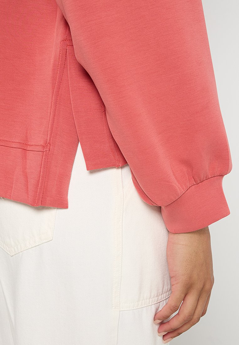 Korallen Sweatshirt mit lässiger Passform, langen Ärmeln, gerippten Bündchen und seitlichen Schlitzen. Aus weichem Stoff mit glatter Textur gefertigt.