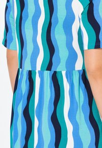 Vestido de manga corta con un patrón ondulado en tonos de azul, verde y blanco, con una cintura fruncida y un corte relajado.