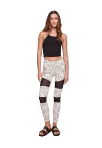Svart avkortet halterneck-top kombinert med hvite leggings med svart blomsterdesign og gjennomsiktige mesh-paneler. Svart sandaler.