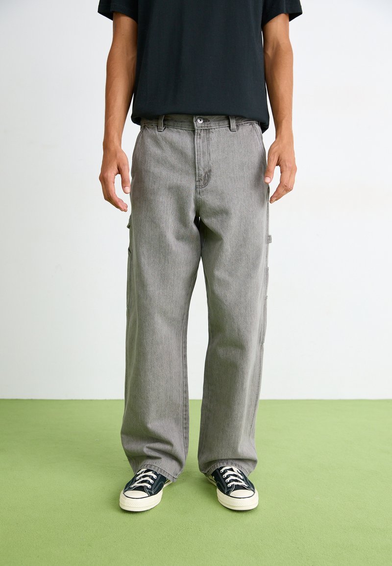 Gray cargo pants with a loose fit, featuring side pockets, a straight leg design, and front button closure. Worn with black sneakers.